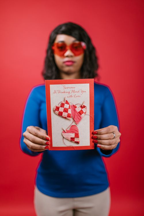 Free A woman wearing red heart-shaped glasses holds a Valentine's card featuring red and white hearts. Stock Photo
