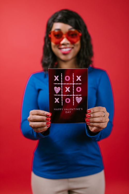 Free A woman holds a Valentine's Day card with tic-tac-toe design against a red background. Stock Photo
