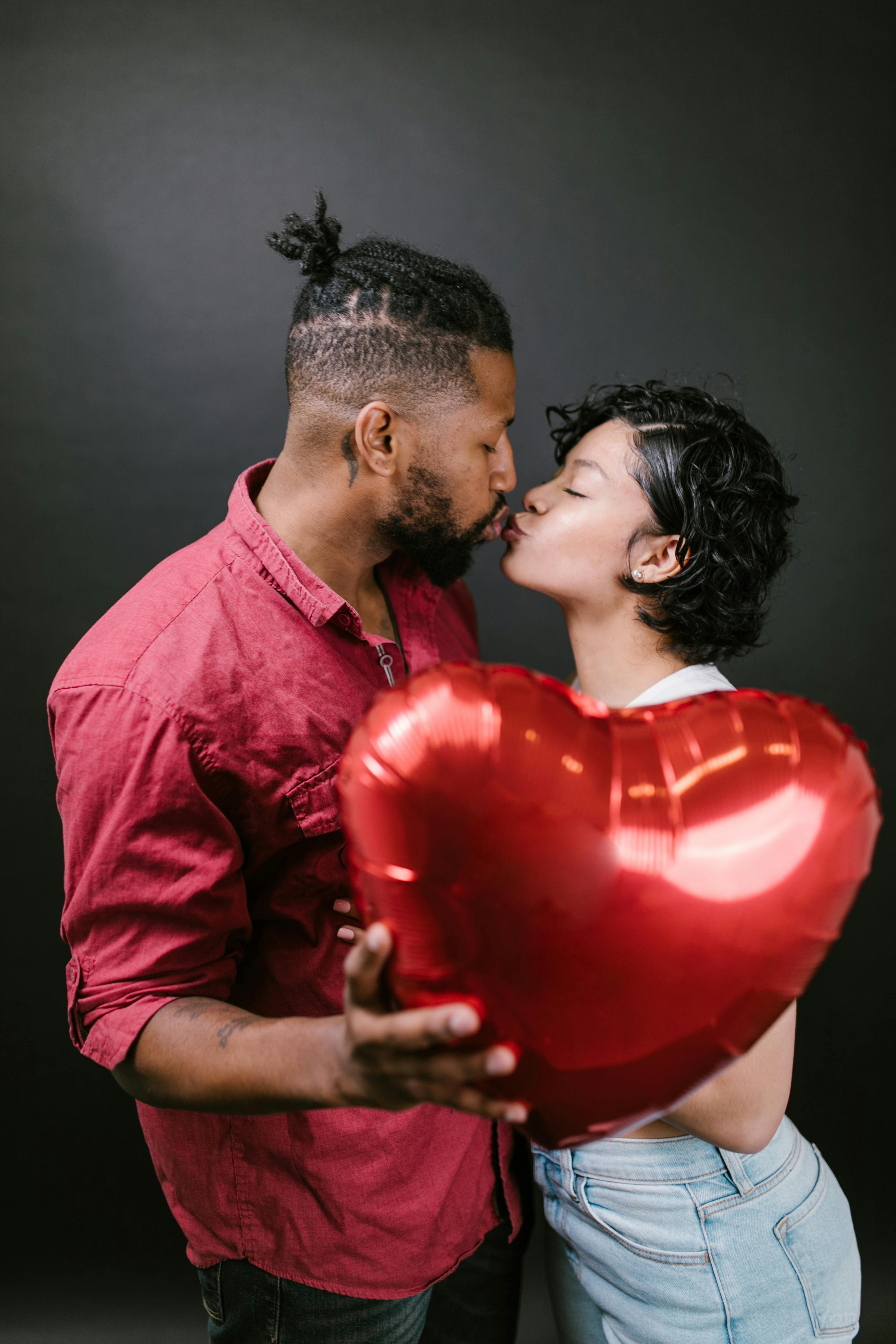 couple kissing while holding a red heart shaped balloon
