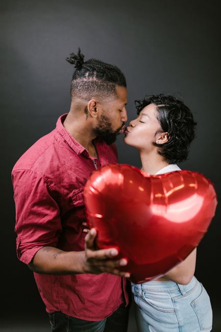 Fotomural Pareja besándose, sosteniendo un globo rojo en forma de corazón sobre un fondo negro.