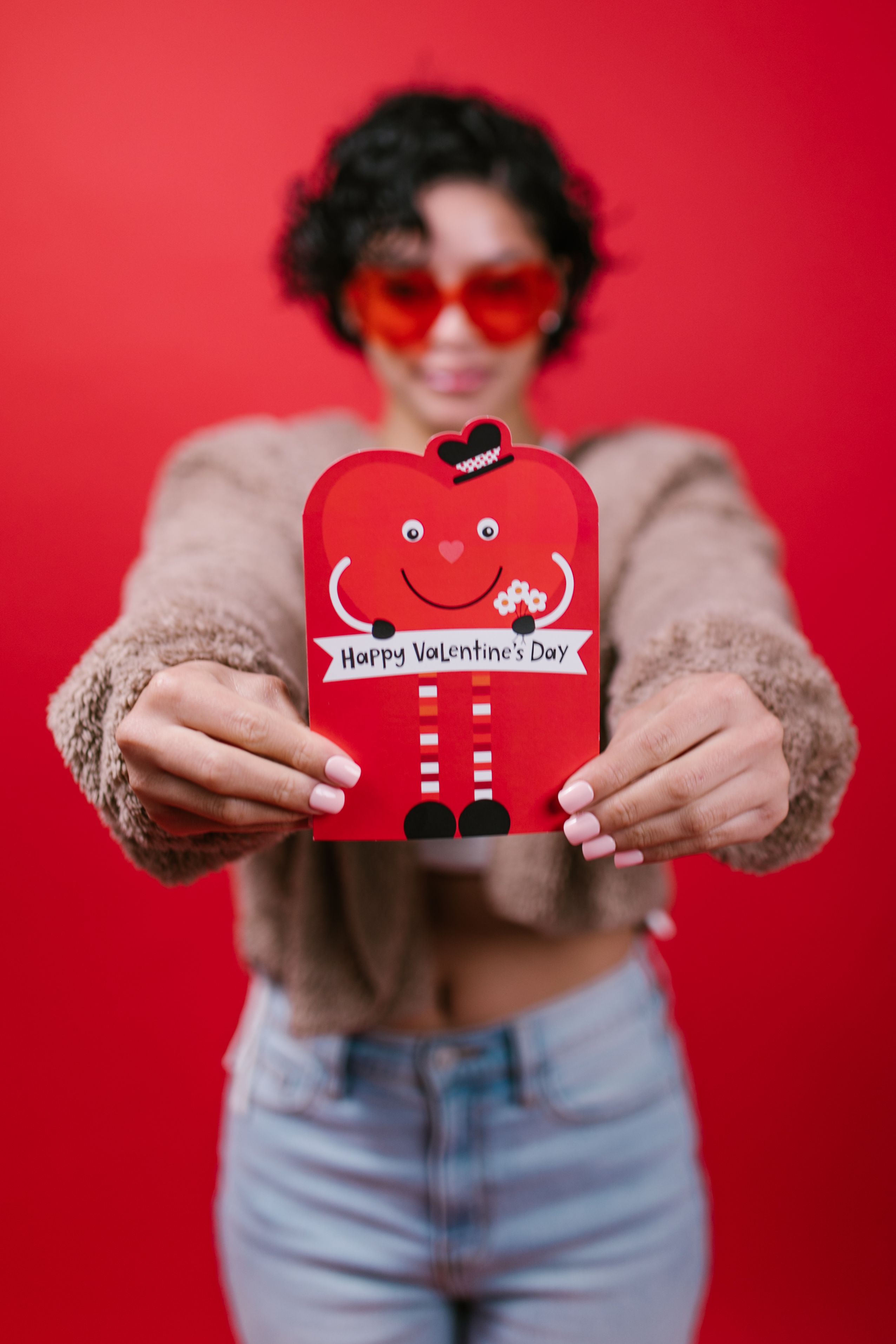 A pair of hands holding a festive Valentine's Day card against a bright red background.
