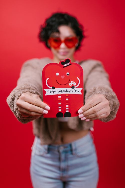 Free A pair of hands holding a festive Valentine's Day card against a bright red background. Stock Photo