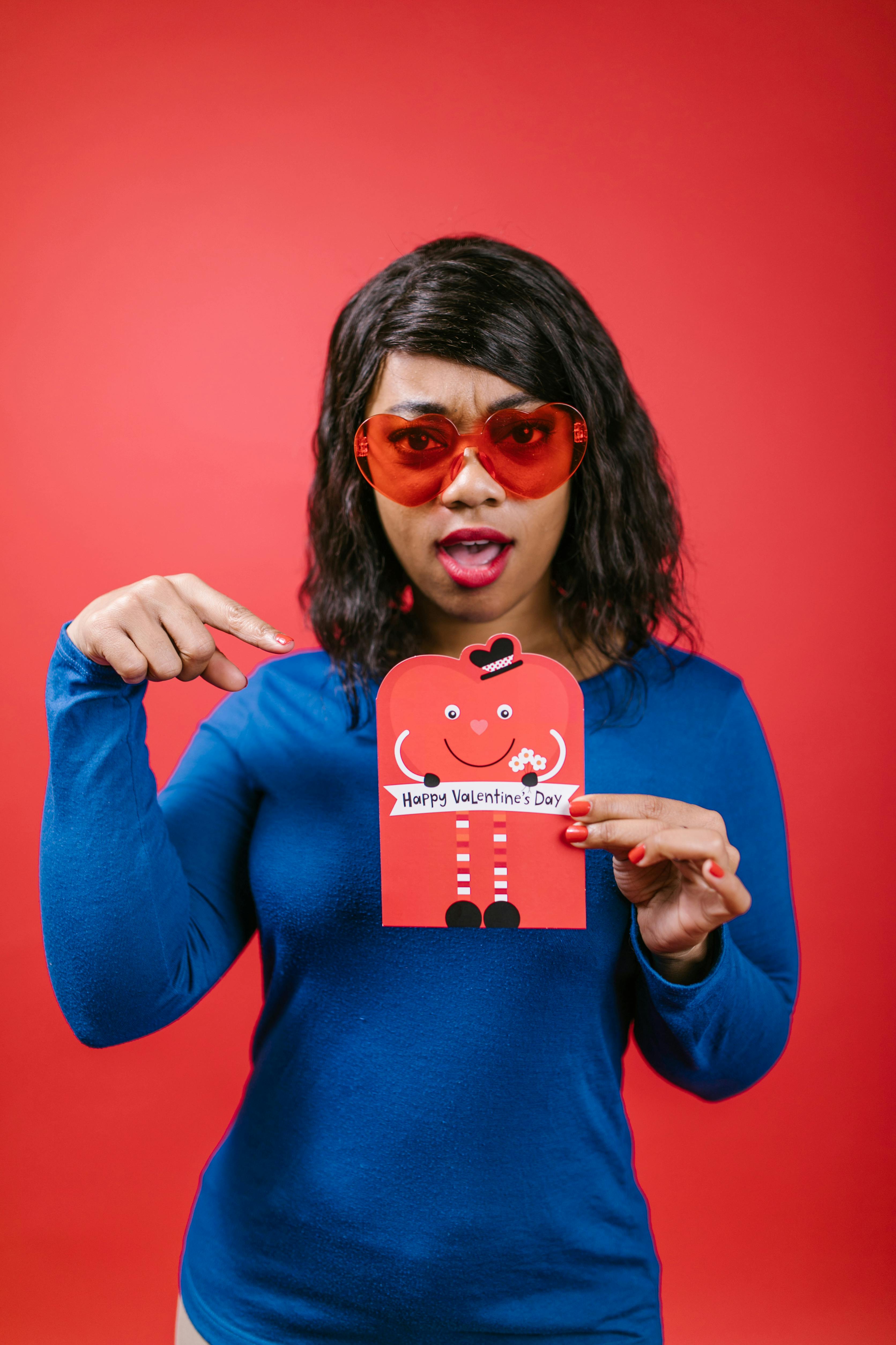 Black woman wearing sunglasses holding a Valentine's Day card against a red background.