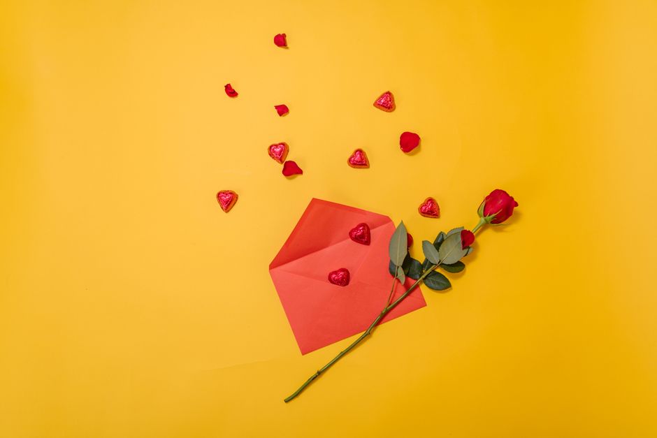Um cenário romântico com uma rosa vermelha, envelope e doces em forma de coração sobre um fundo amarelo.
