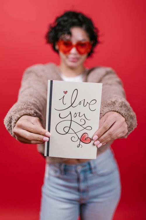 Free Woman holding a Valentine's card with an 'I Love You' message in front of a red background. Stock Photo