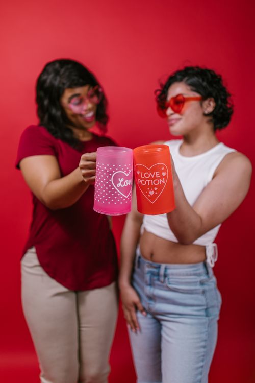 Free Two women celebrating with love-themed mugs against a red background, perfect for Valentine's Day. Stock Photo