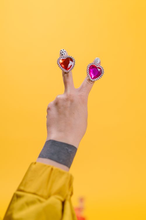 Free A hand displays a peace sign with heart-shaped rings on a vibrant yellow background. Stock Photo