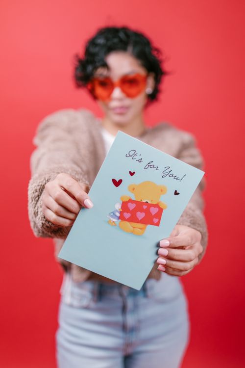 Free Woman holding a Valentine's card with a teddy bear, on a vibrant red background. Stock Photo