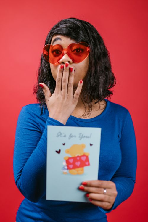 Free Woman in blue shirt surprised with Valentine's card and heart-shaped sunglasses. Stock Photo