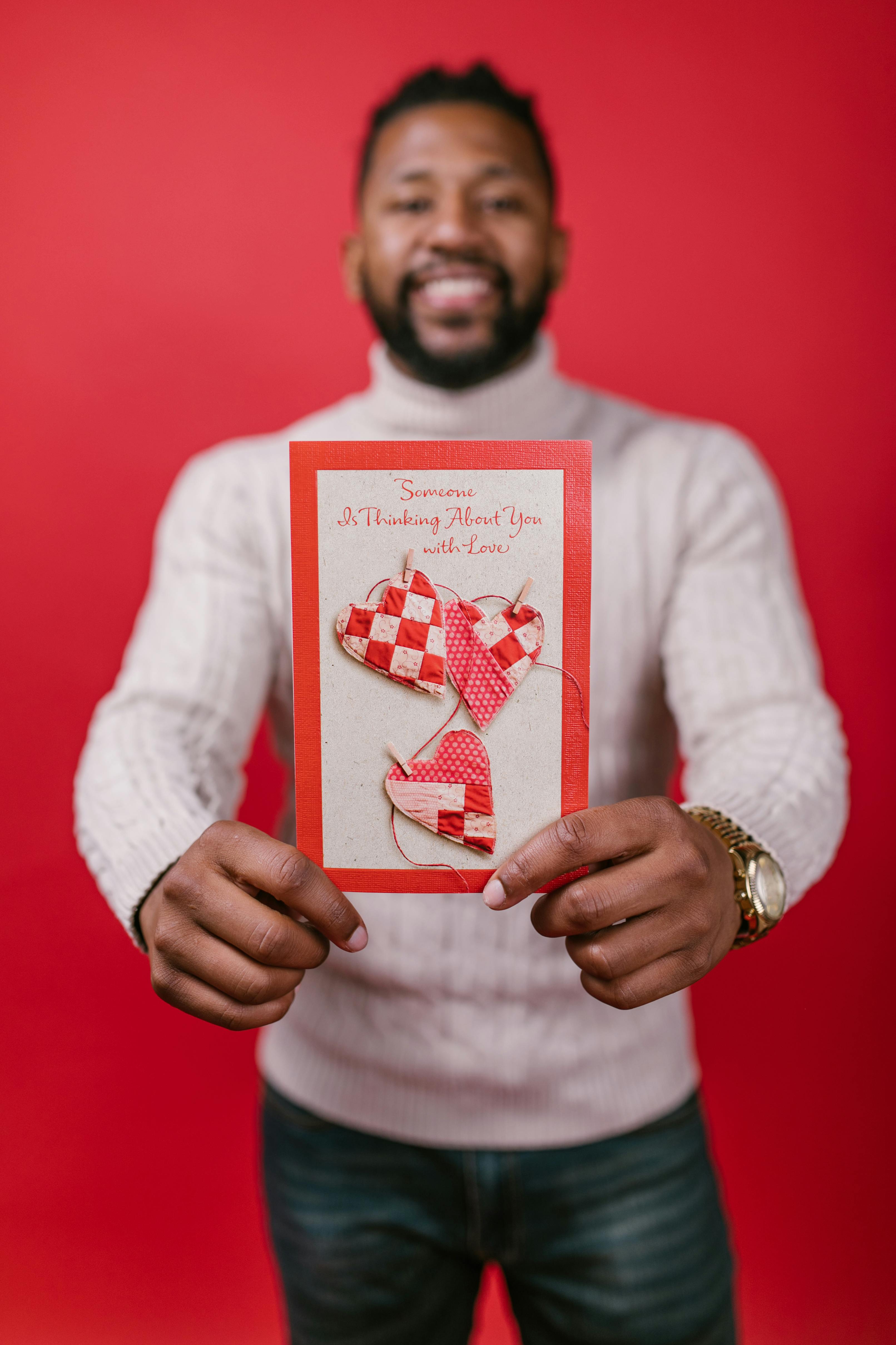Smiling man holding Valentine's Day card with hearts on red background.