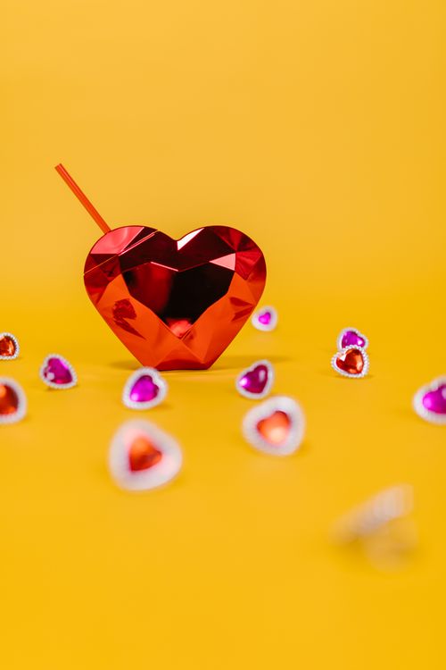 Free A vibrant red crystal heart with smaller colorful hearts against a yellow background. Stock Photo