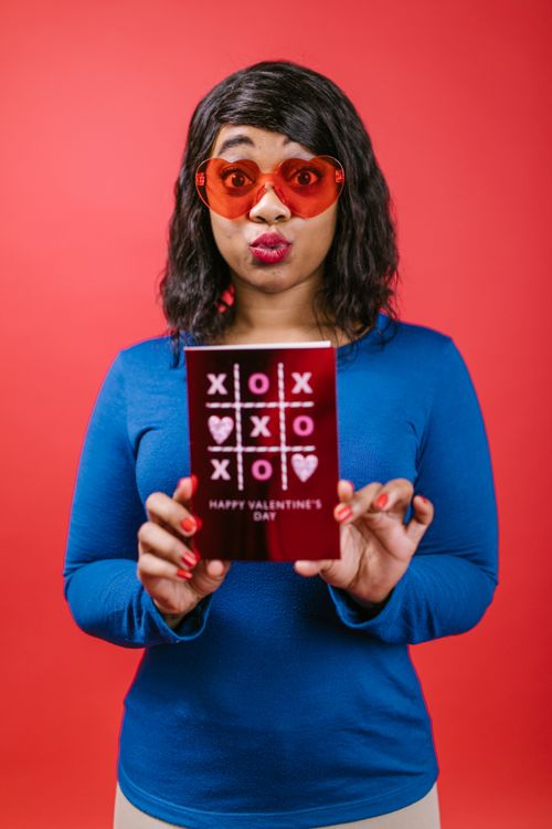 Free Woman with red sunglasses holding Valentine's card, playful expression. Stock Photo