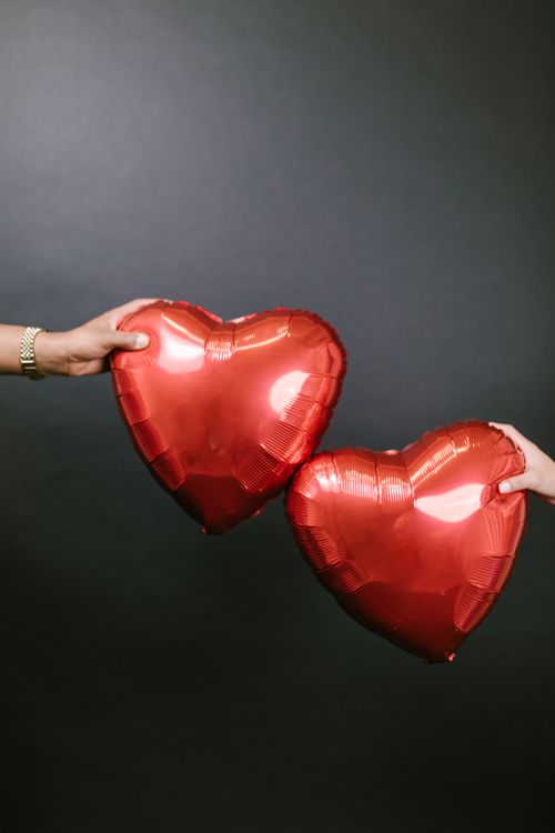 Free Two hands holding red heart-shaped balloons against a dark background symbolizing love and romance. Stock Photo