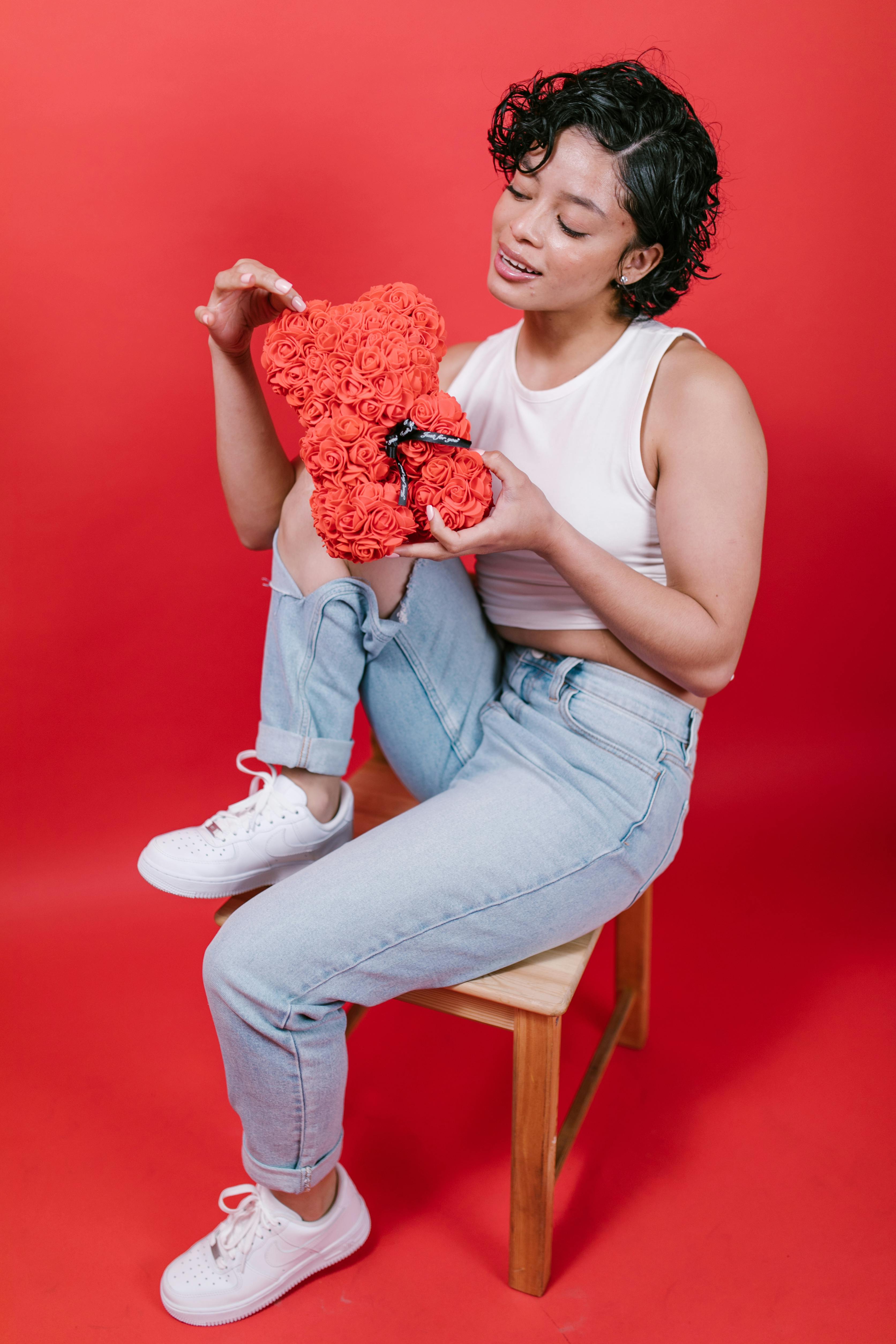 Young woman sitting with rose teddy bear on red background, perfect for Valentine's themes.