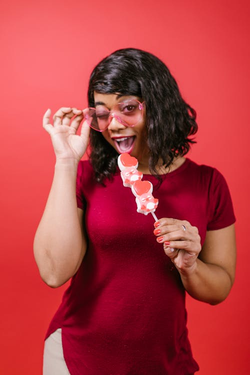 Woman in Red Crew Neck Shirt Holding Candies in a Stick