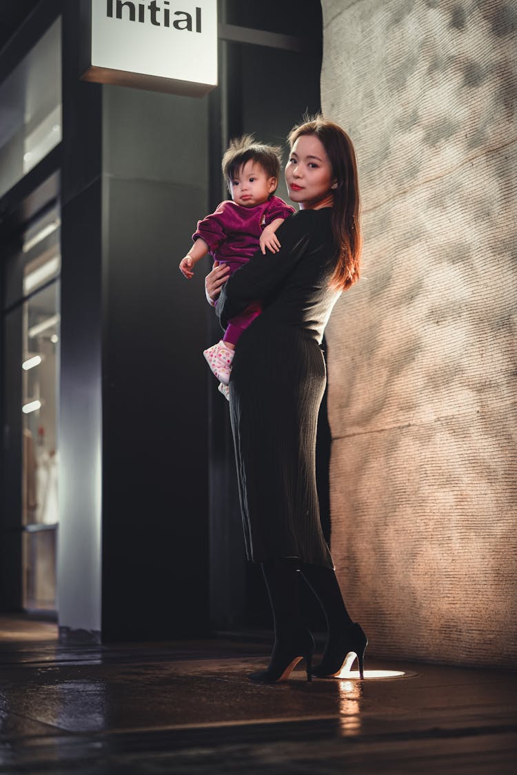 Woman In Black Long Sleeve Dress Carrying Her Baby