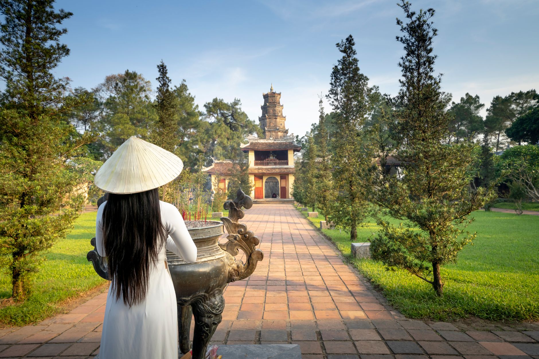 Back view of anonymous female in hat standing near green trees and pathway leading to old Pagoda Of The Celestial Lady