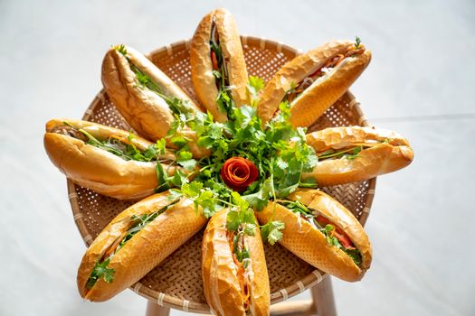 Top view of delicious sandwiches with fresh prosciutto and green herbs arranged on wicker tray in light room at home