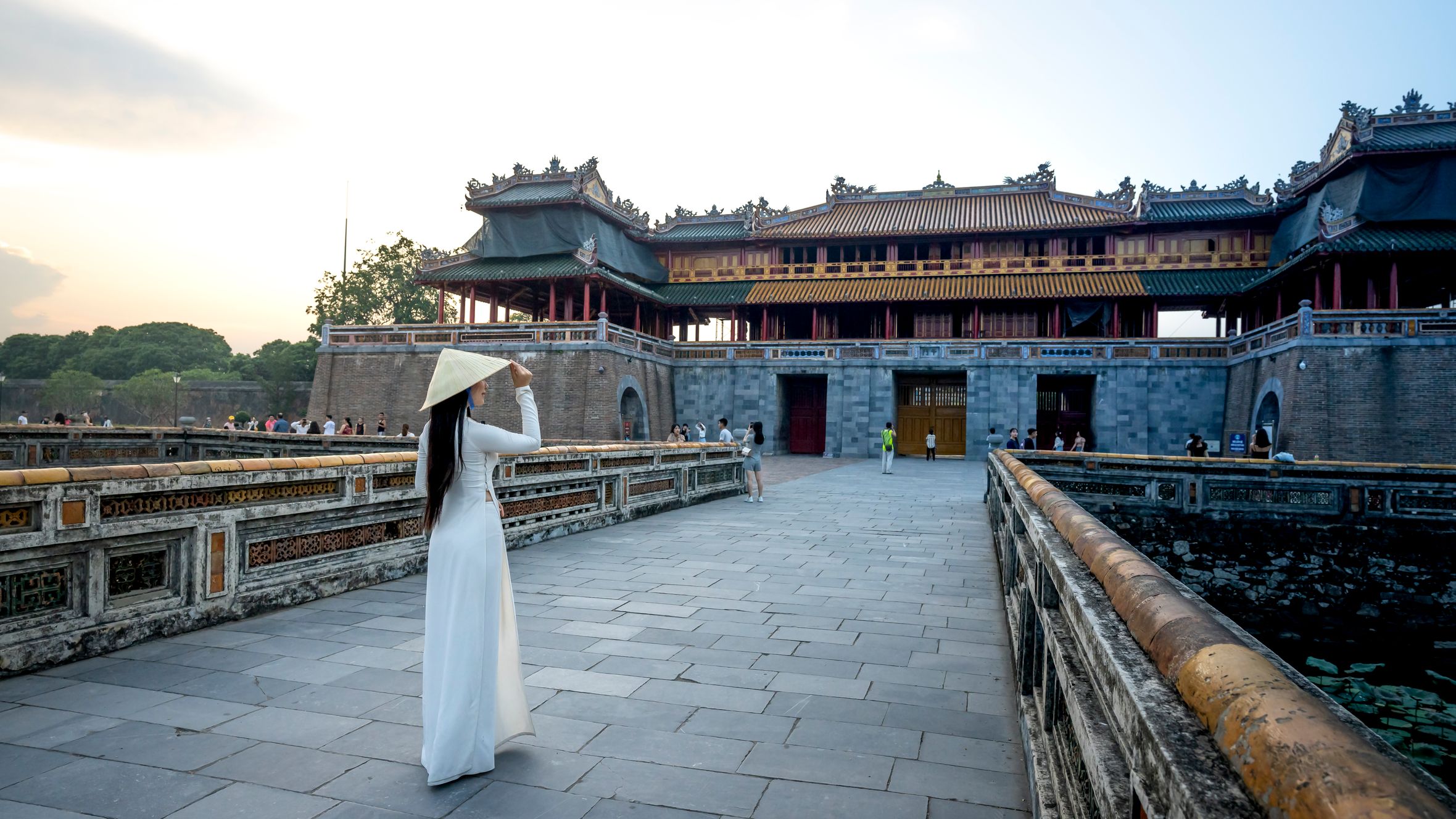 Full body back view of anonymous female wearing hat and dress strolling against meridian gate located in city of Vietnam