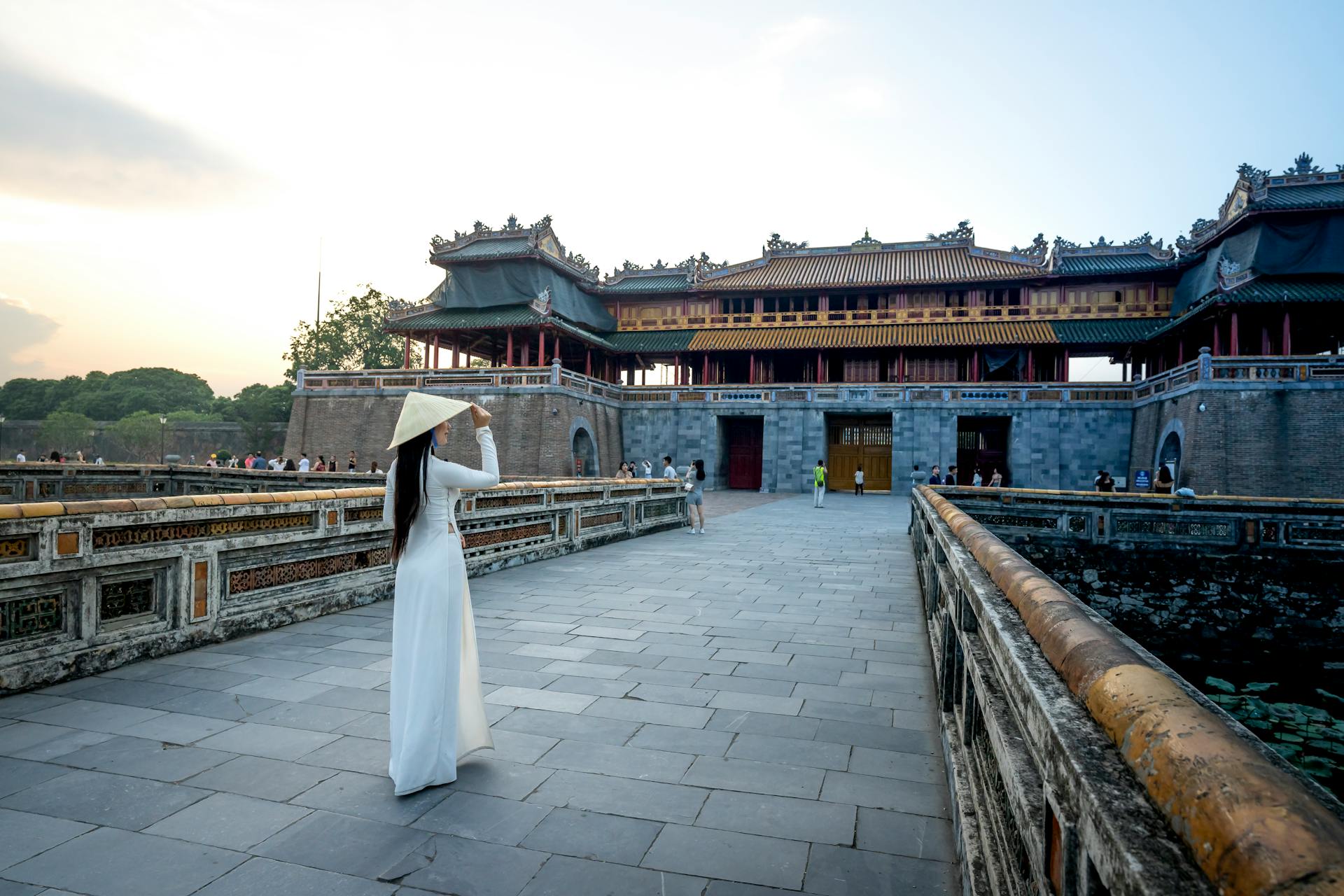 Full body back view of anonymous female wearing hat and dress strolling against meridian gate located in city of Vietnam