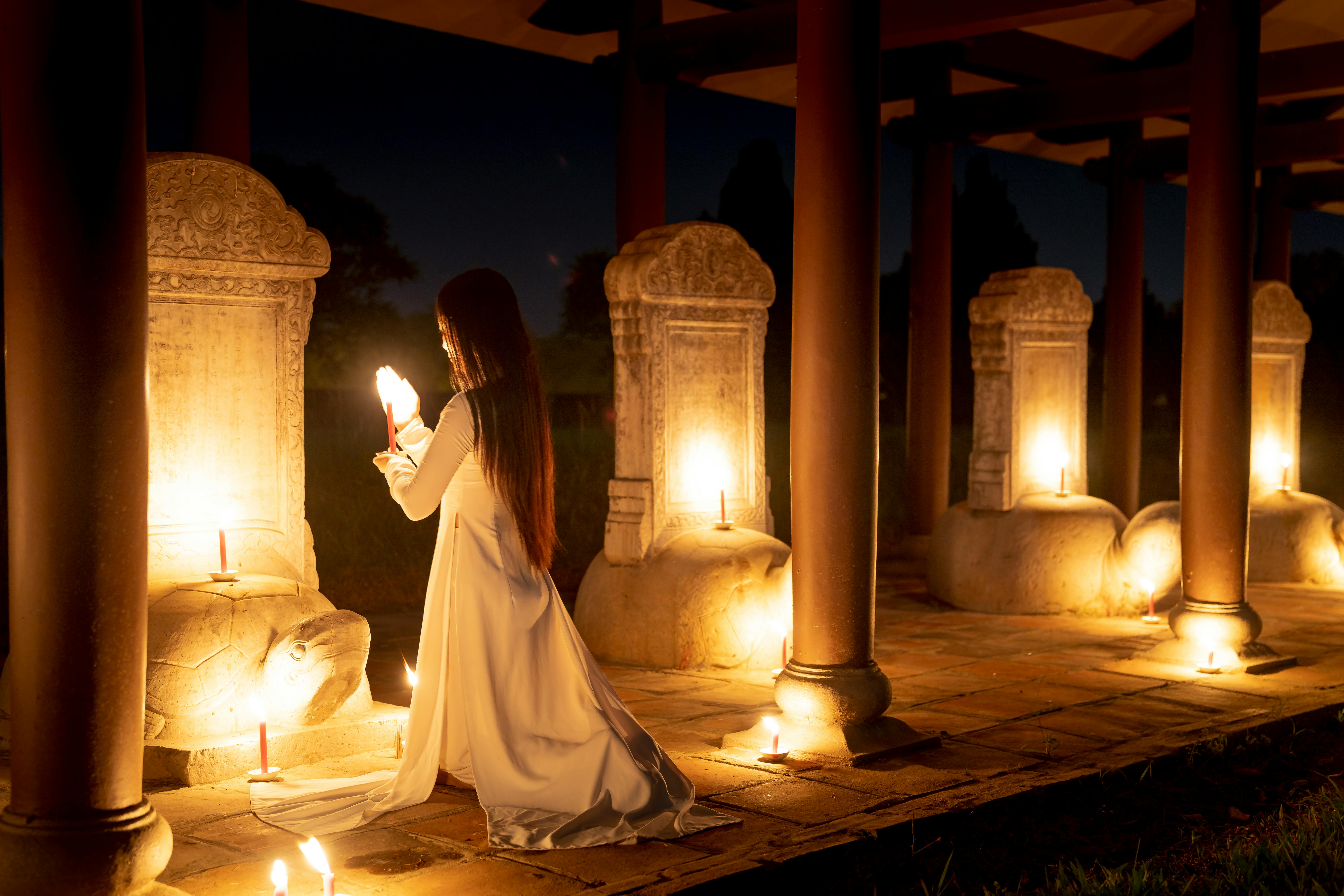 unrecognizable woman with candle praying near stele