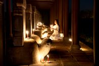 Side view of tranquil Asian female with burning candle in hands praying near stone turtles with steles in dark time