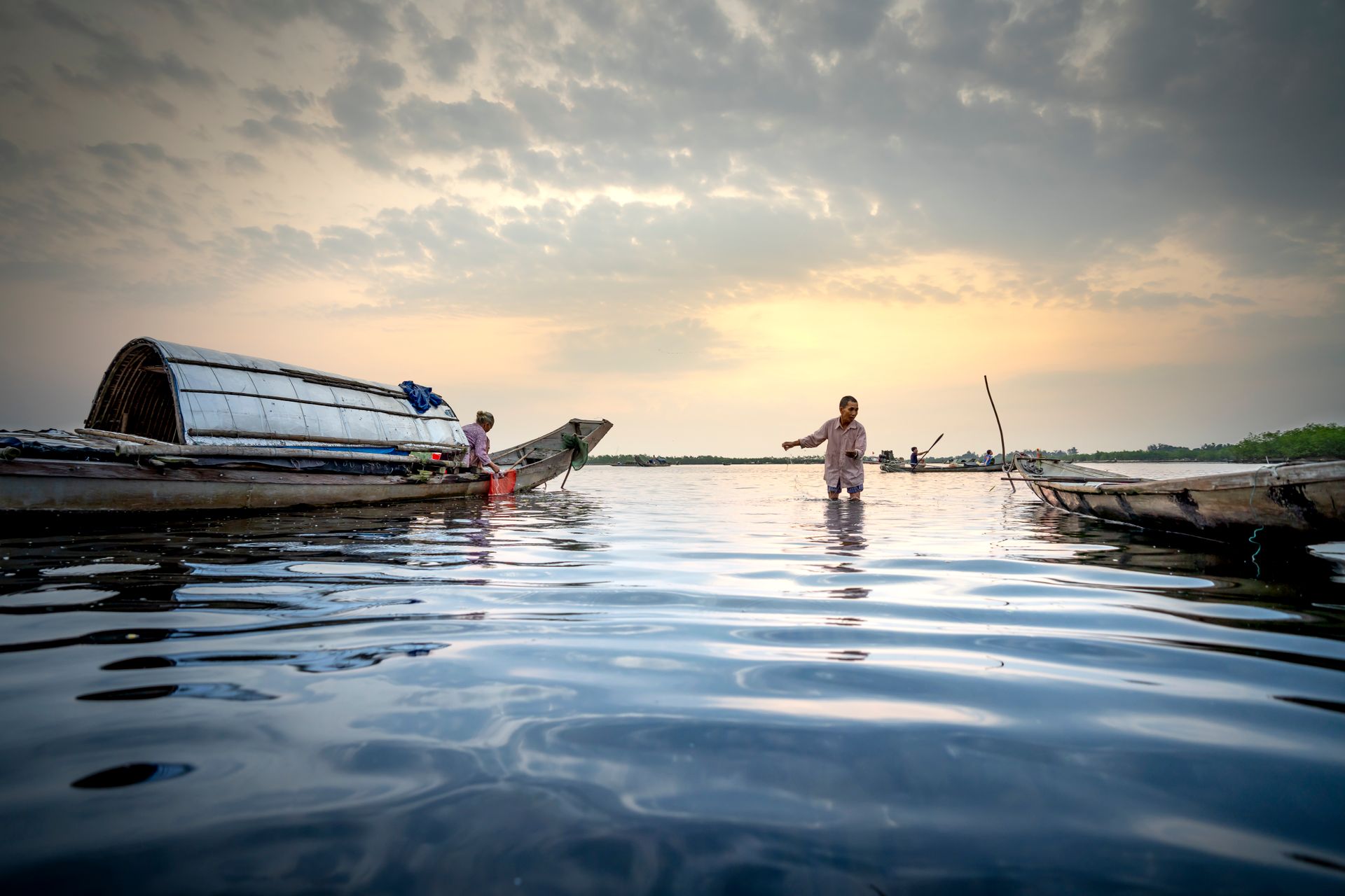 People of local village with fishing equipment on boat in shallow water under cloudy sky
