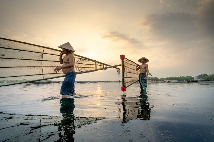 Asian Fishermen In Vietnamese Hats With Fishing Net In River