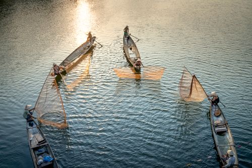 Free From above of anonymous men in boats fishing with nets in rippled ocean with shiny water in evening Stock Photo