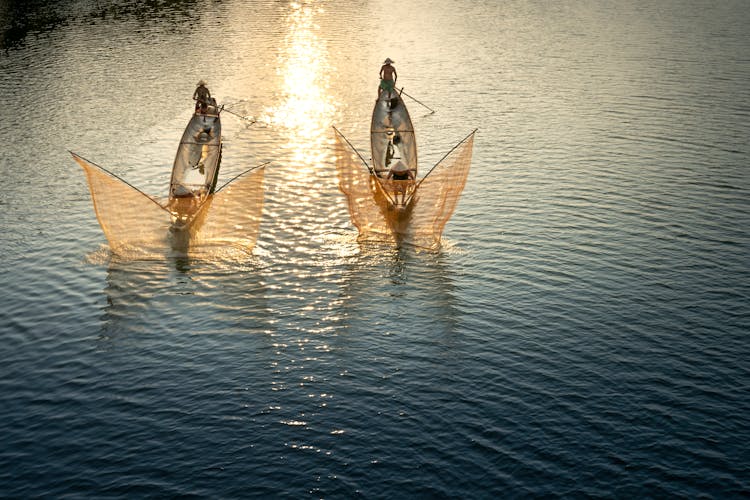 Unrecognizable Fishermen In Boats Catching Fish With Nets In Ocean