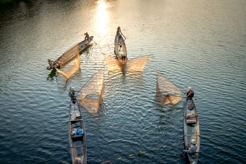 Free Drone view of unrecognizable male partners in oriental boats fishing with nets in rippled sea with shiny water Stock Photo