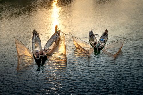 Free From above of anonymous men in boats fishing with nets in rippled ocean with shiny aqua in evening Stock Photo