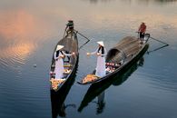 From above of anonymous female speaking in boats with candle lanterns against male partners with paddles in boats on river