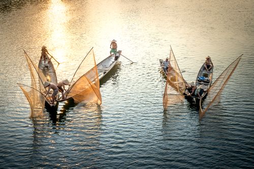 Free High angle of unrecognizable male partners in conical hats standing in boats with nets while fishing in shiny sea Stock Photo
