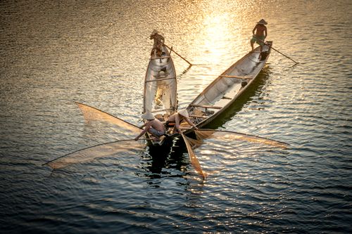 Free From above of anonymous shirtless men in oriental hats fishing with nets in sea from boats in sunlight Stock Photo