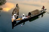 From above of anonymous female talking in boats against male with paddles sailing on lake during lantern festival in twilight