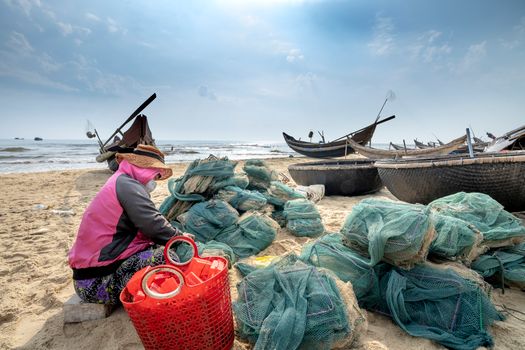 Anonymous ethnic woman tying fishing net on sea shore