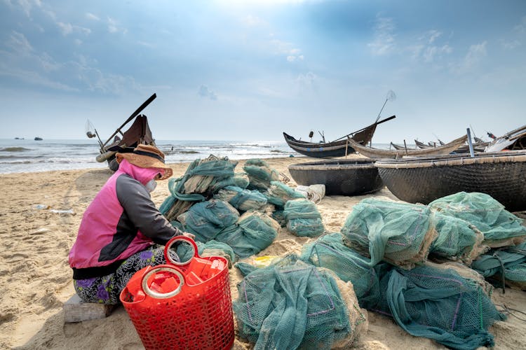 Anonymous Ethnic Woman Tying Fishing Net On Sea Shore