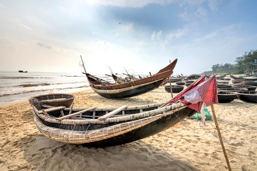 Old oriental boats on coast with footprints against endless ocean under cloudy sky in sunlight