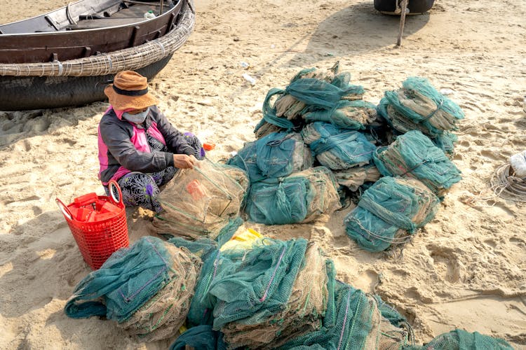 Unrecognizable Ethnic Woman Tying Net On Sandy Coast