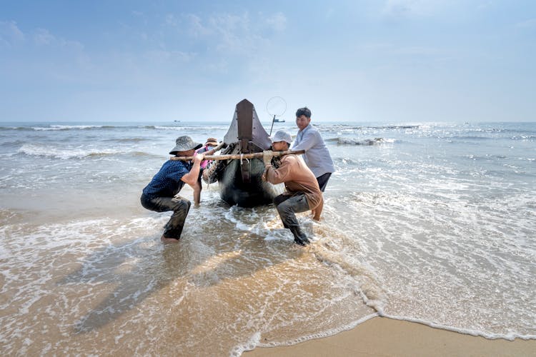 Unrecognizable Asian Fishermen Pulling Boat On Wavy Sea In Sunlight