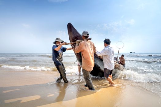 Unrecognizable ethnic fishermen pulling boat on sea shore