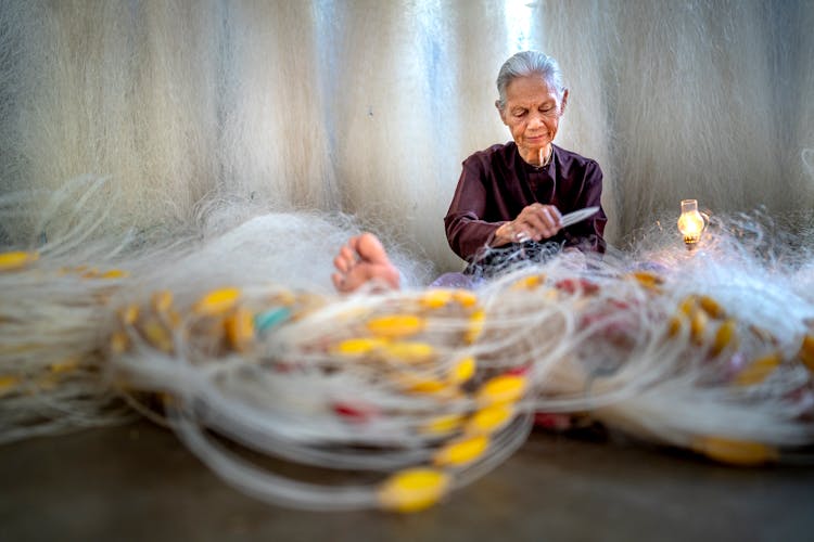 Elderly Asian Woman Repairing Fishing Net Against Lamp