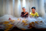 Ethnic grandmother with needle weaving fishing net against boy