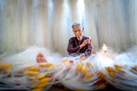 Old Asian woman mending fishing net against kerosene lamp