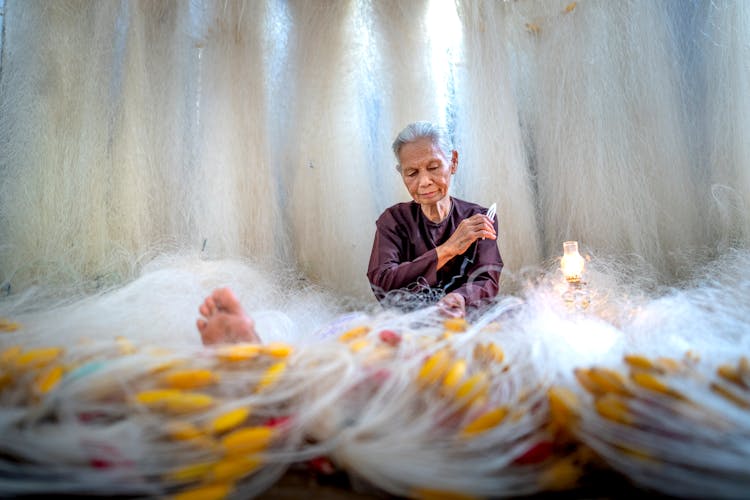 Old Asian Woman Mending Fishing Net Against Kerosene Lamp