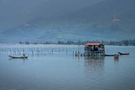 Side view of anonymous fisherman in boat catching fish in rippled lake against aged construction and ridge
