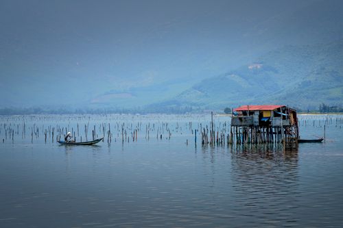 Free Side view of anonymous male fisher sailing in boat on rippled lake against old construction and ridge Stock Photo