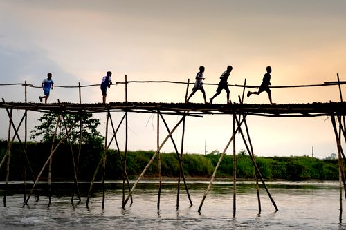 Free Unrecognizable active ethnic kids jogging on footbridge above lake while working out under sunset sky Stock Photo