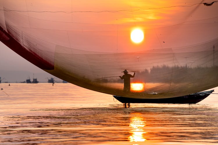 Anonymous Fisherman Catching Fish From Boat In River At Sundown